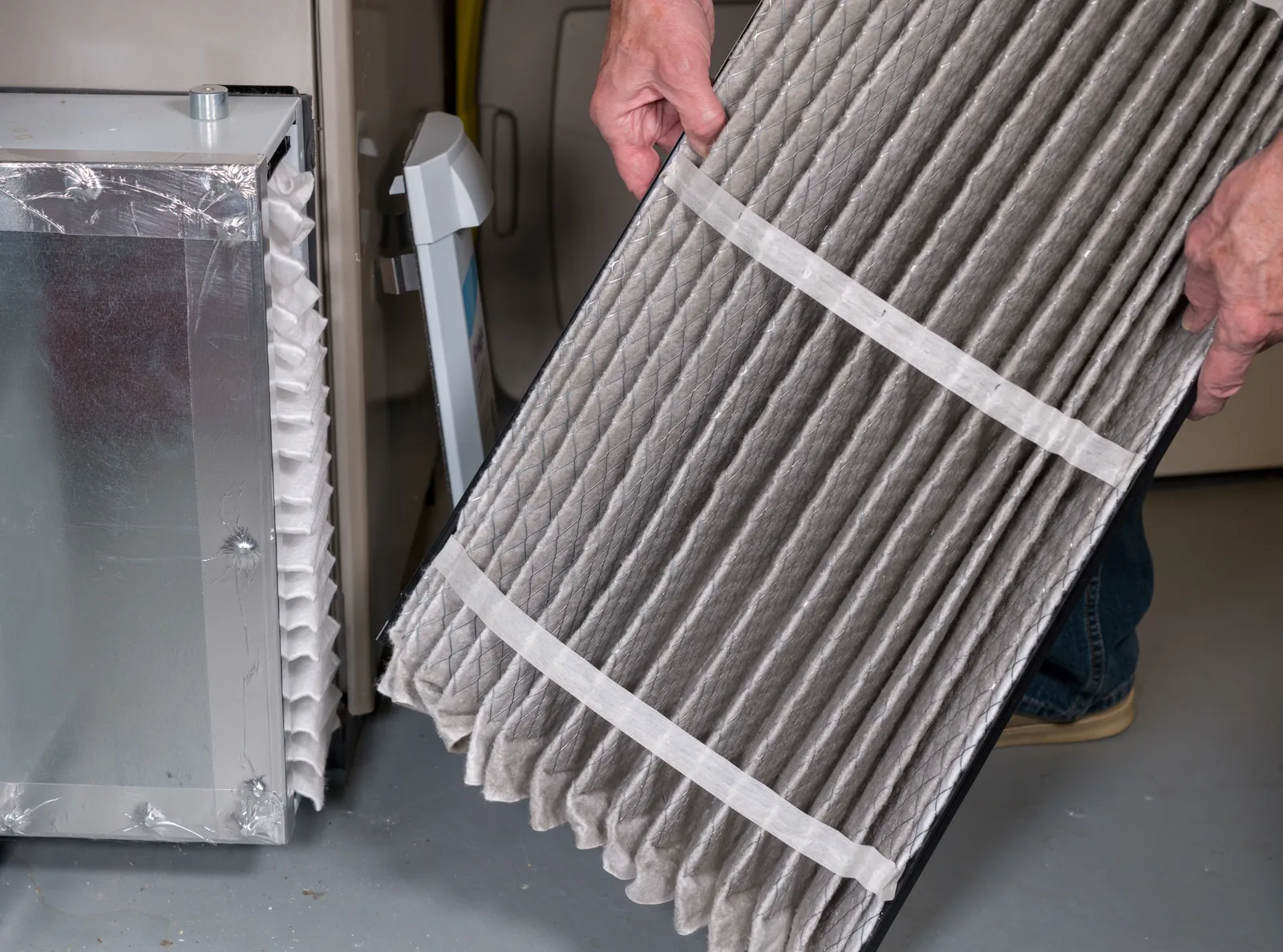 Hands pulling a used pleated air filter out of a home furnace so a fresh one can go in